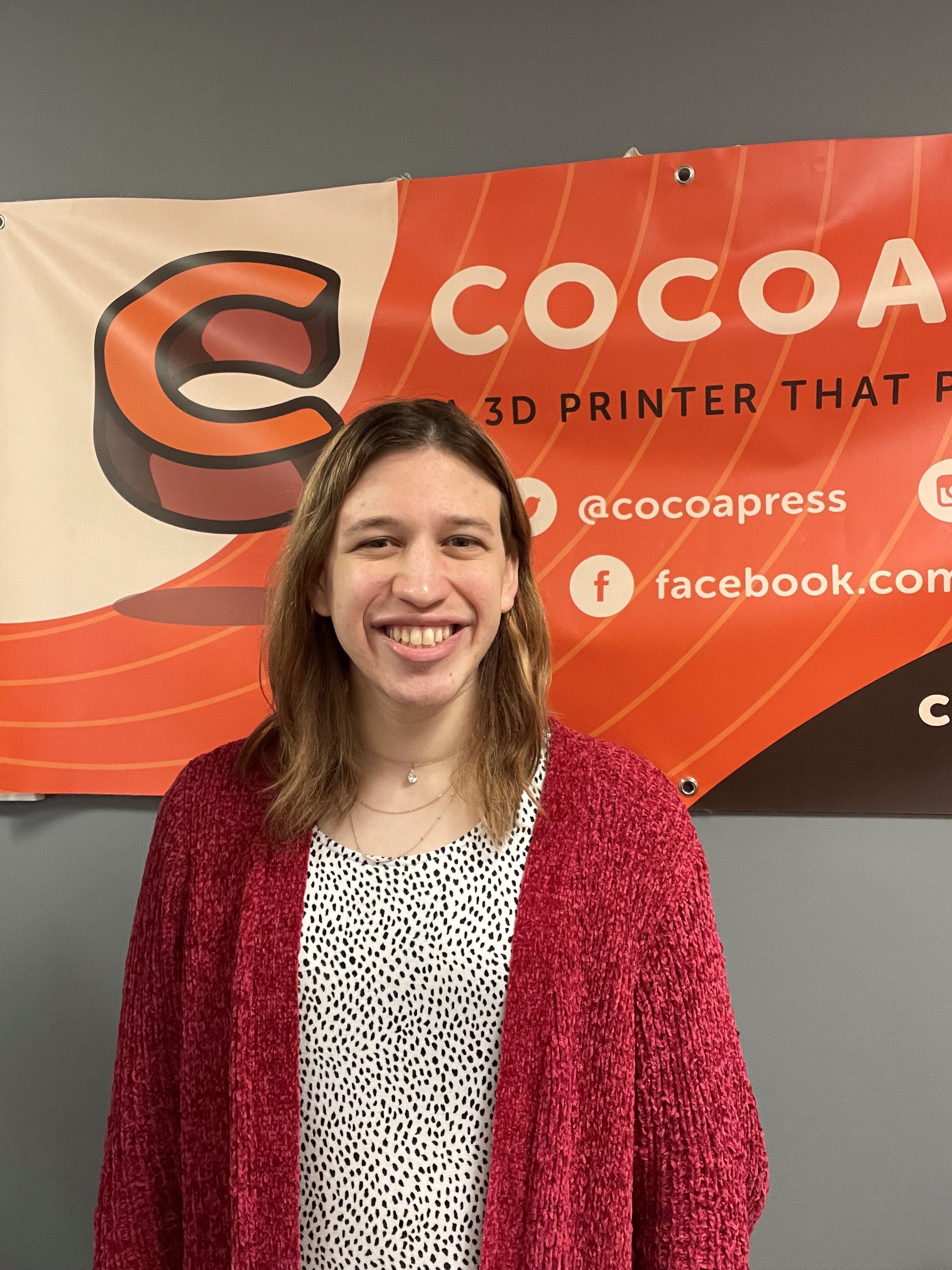 Cocoa Press Founder standing in front of Cocoa Press banner